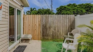 A backyard with a wooden fence, a small patio with two chairs, and a green artificial turf area. - Al Capone - Paradise Apartment (Cape Coral)
