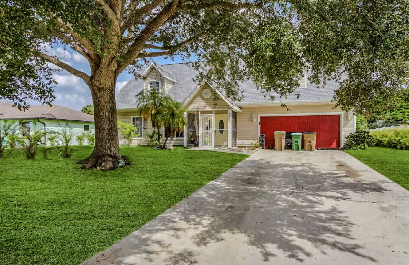 A two-story house with a red garage, a large tree in front, and a well-maintained lawn.