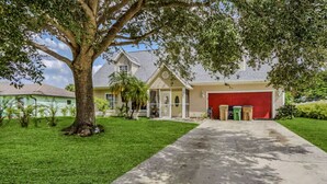 A two-story house with a red garage, a large tree in front, and a well-maintained lawn. - Al Capone - Paradise Apartment (Cape Coral)