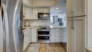 A modern kitchen with white cabinetry, stainless steel appliances, and a patterned rug. - Top Floor Ocean View! | Island Club 1502 (Hilton Head Island)