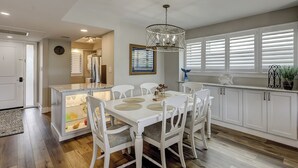 A modern kitchen with white cabinetry, a central island with glass front, and a dining area with white chairs and a table. - Top Floor Ocean View! | Island Club 1502 (Hilton Head Island)