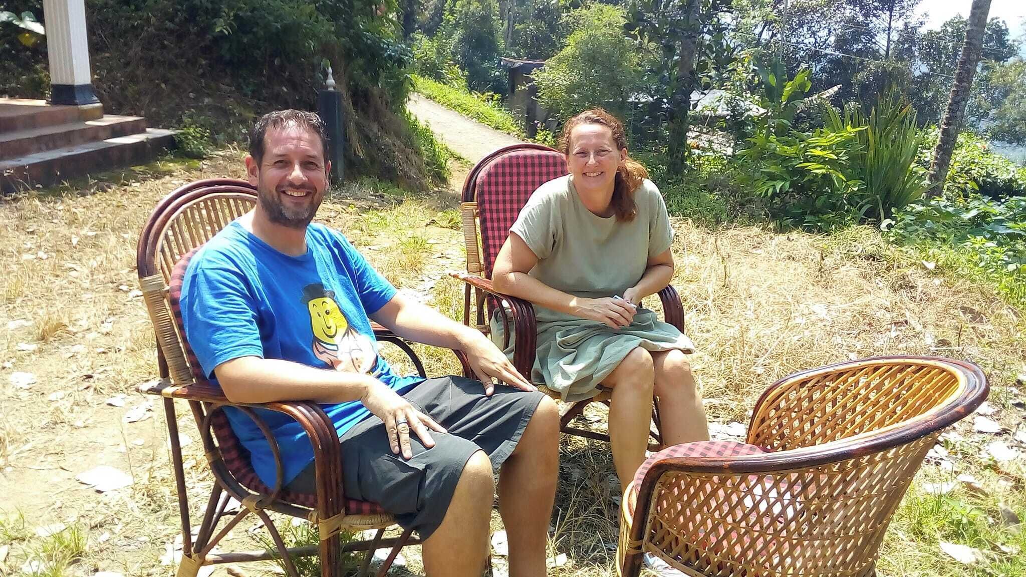 Two people seated on wicker chairs outdoors with a natural backdrop.