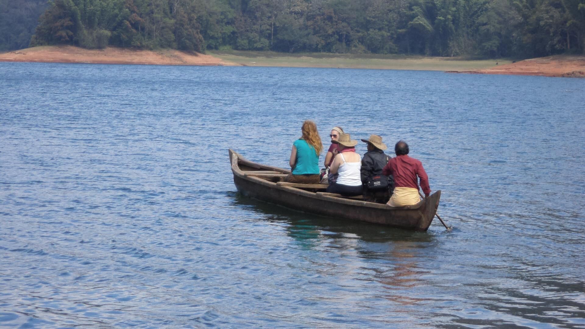 A group of people in a wooden boat on a calm lake.