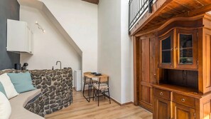 A cozy room with a stone wall, a wooden dining table with chairs, a white sofa, and a wooden cabinet with glass doors. - 200m Monastero Benedettini Loft in historic center (Catania)
