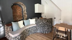 Une pièce chaleureuse avec un mur en pierre, un canapé incurvé agrémenté de coussins, une table en bois et un meuble blanc.