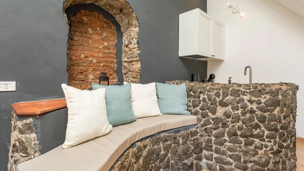 A stone bench with cushions, a stone wall, a white cabinet, and a sink.