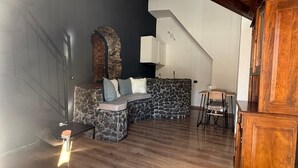 A spacious loft with a high ceiling, exposed wooden beams, a stone fireplace, and a dining area. - Jesuit Home - Lumina Collection (Catania)