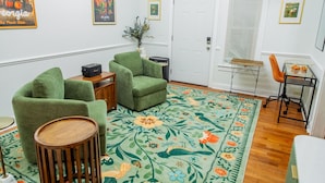 A living room with green armchairs, a wooden coffee table, a floral rug, a small side table, and a radio. - Historic Westend Jewel-Pet Friendly, Sleeps 12 (Atlanta)