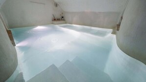 Quarto com uma banheira grande e transparente, uma pequena prateleira com objetos decorativos e teto inclinado.