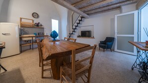 Un'area pranzo con tavolo e sedie in legno, una cucina con lavello e fornello, una scala e un televisore appeso al muro.