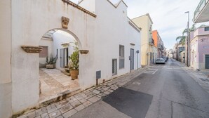 Una stretta via con edifici bianchi, un marciapiede lastricato e alcune auto parcheggiate.