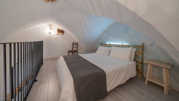 Quarto com cama, uma cadeira, um banco de madeira e um teto curvo singular.