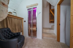 Une pièce avec un fauteuil en cuir noir, un escalier en bois et une porte illuminée d’une lumière violette.