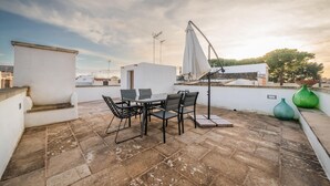 Una terrazza sul tetto con tavolo e sedie, un ombrellone bianco e un vaso verde.