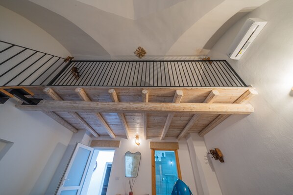 Un balcon en bois avec une balustrade, un plafond avec des poutres apparentes et un climatiseur fixé au mur.