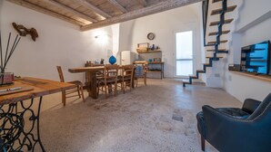 Ampla sala de estar com mesa de jantar de madeira, cadeiras, sofá azul e escada para um andar superior.