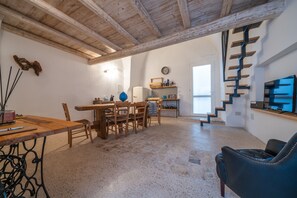 A spacious living area with a wooden dining table, chairs, a blue sofa, and a staircase leading to an upper level. - Amazing Apartment "Alla Corte" with pool and sauna (Taurisano)
