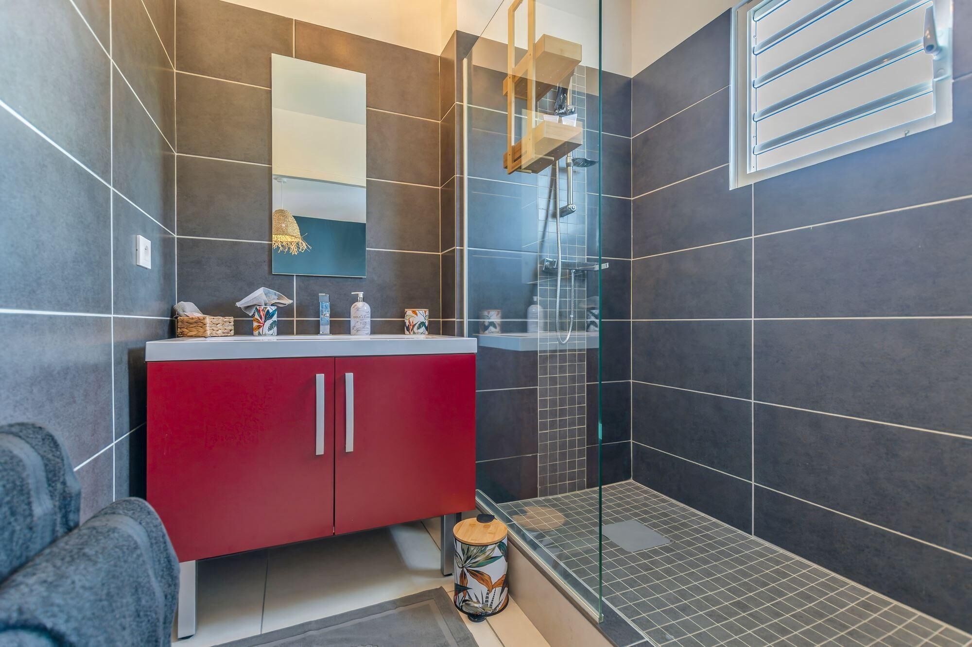 Un baño moderno con un mueble rojo, cerramiento de ducha de vidrio y un espejo grande.