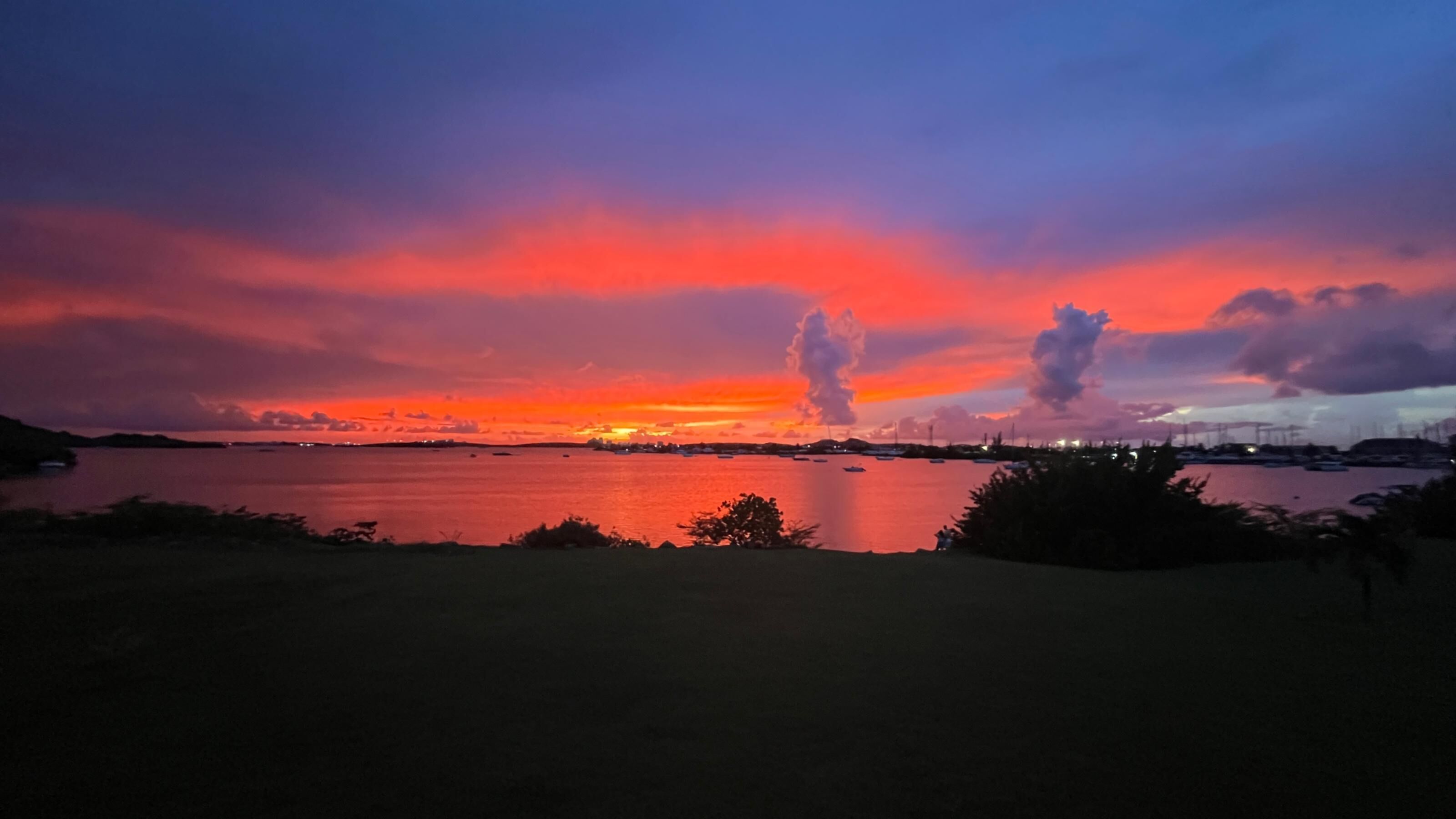 A sunset over a calm body of water with distant land and boats.