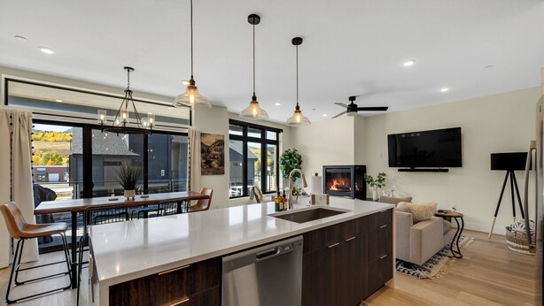 A modern kitchen with a large island, built-in dishwasher, pendant lighting, and a flat-screen TV. - Newly Constructed Condo along the Blue River (Silverthorne)