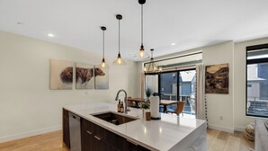 A modern kitchen with a central island, pendant lighting, and artwork on the walls. - Newly Constructed Condo along the Blue River (Silverthorne)
