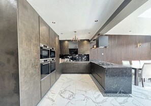 Une cuisine moderne avec des meubles de rangement aux couleurs foncées, un plan de travail en marbre et un four encastré.