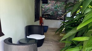 A covered outdoor seating area with wicker furniture, a large planter with green foliage, and a concrete floor. - Romantic Tiny Farmhouse Retreat with AC & Pool in Corozal (Corozal)