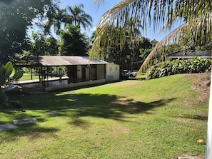 A covered outdoor area with a pathway leading to a building, surrounded by greenery and palm trees. - Romantic Tiny Farmhouse Retreat with AC & Pool in Corozal (Corozal)