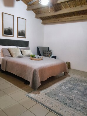 A bedroom with a bed, a chair, a rug, and two framed pictures on the wall. - Romantic Tiny Farmhouse Retreat with AC & Pool in Corozal (Corozal)
