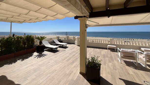 A covered outdoor area with lounge chairs and potted plants, overlooking a beach. - CANELA BEACH DREAM, PENTHOUSE ON THE SEA (Isla Canela)