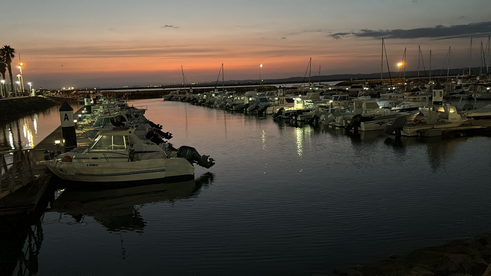 A marina at dusk with boats docked along the waterfront.