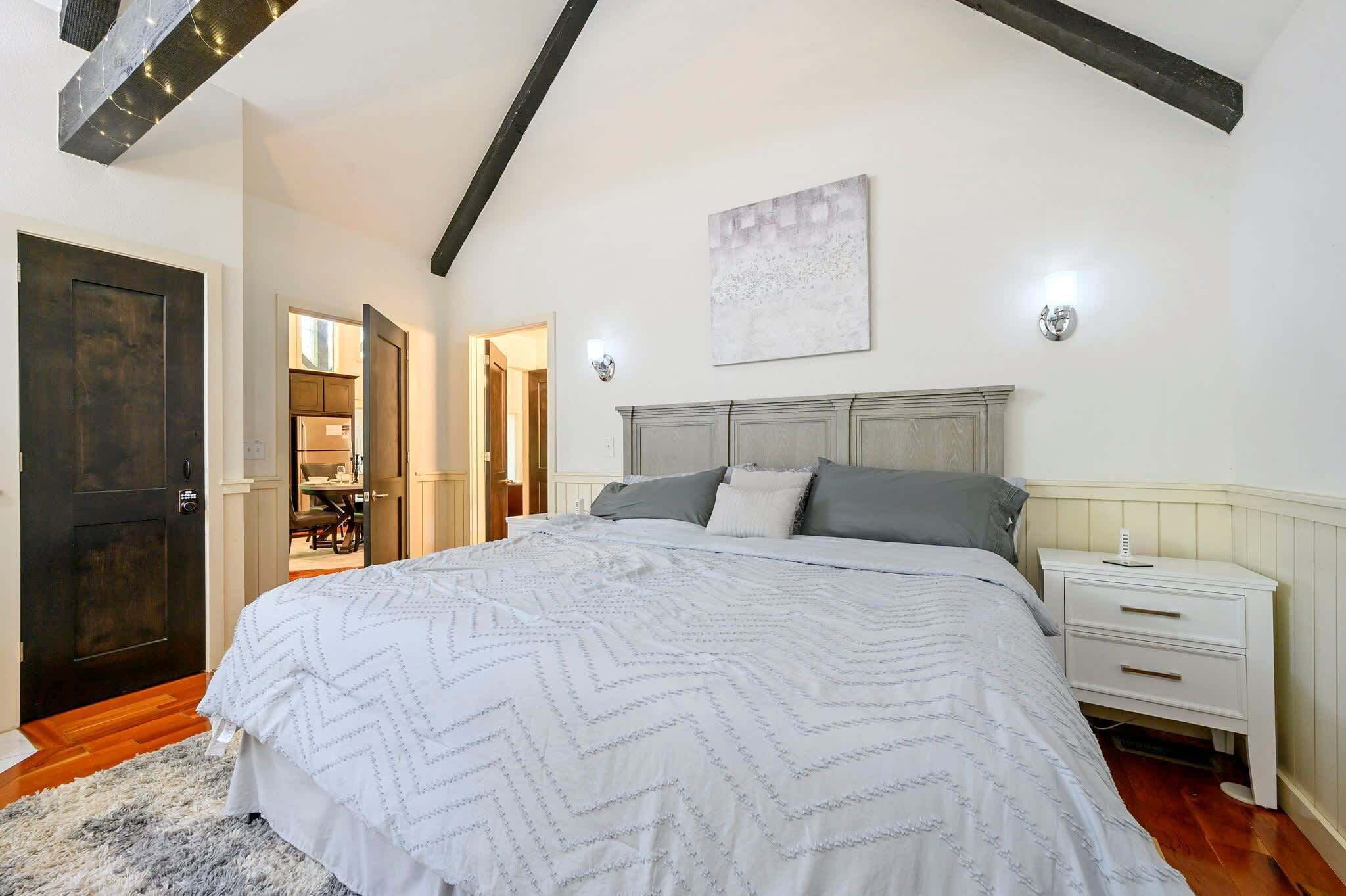 Une chambre avec un grand lit, une table de chevet, une lampe fixée au mur et une porte.