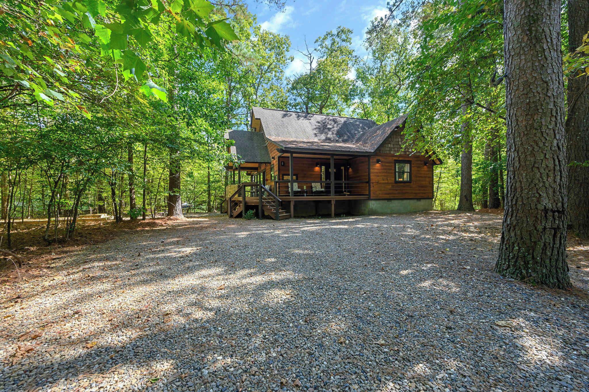 A cabin with a gravel driveway, surrounded by trees.