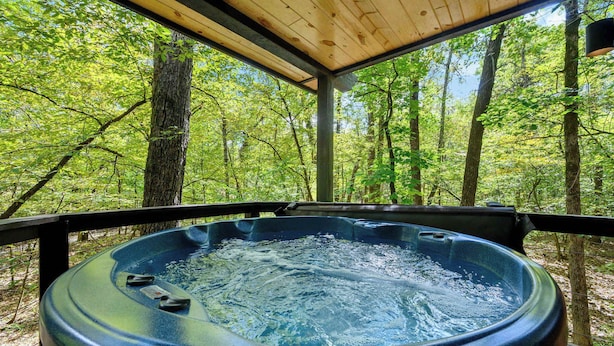 Un bain à remous entouré d’une terrasse en bois, avec vue sur la forêt.
