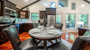 Une cuisine moderne avec des meubles de couleur bois foncé, des appareils électroménagers en acier inoxydable et un coin repas doté d’une table ronde pour quatre personnes.