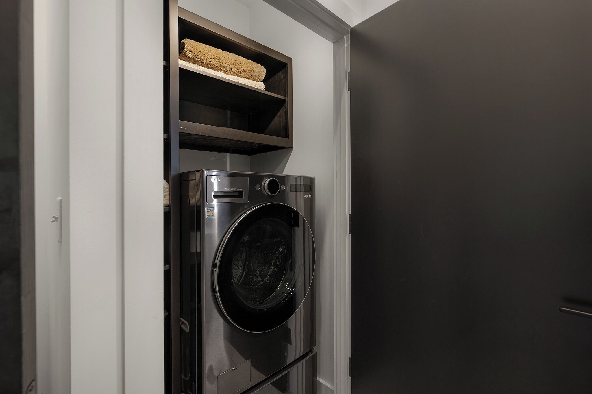 Een kleine wasruimte met een wasmachine en een plank erboven.