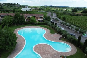 Une piscine au design ondulant, entourée d’une terrasse en briques et d’une végétation luxuriante.