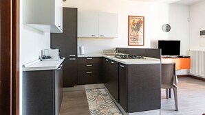 A compact kitchen with dark cabinetry, a white countertop, a gas stove, and a small dining area with a chair.