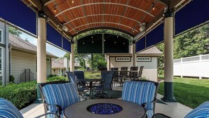 Une terrasse extérieure avec une table ronde, des chaises à rayures bleues et un foyer.