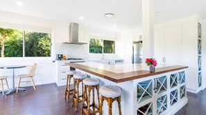 Une cuisine moderne dotée d’un îlot central, de tabourets de bar et offrant une vue sur la verdure environnante.