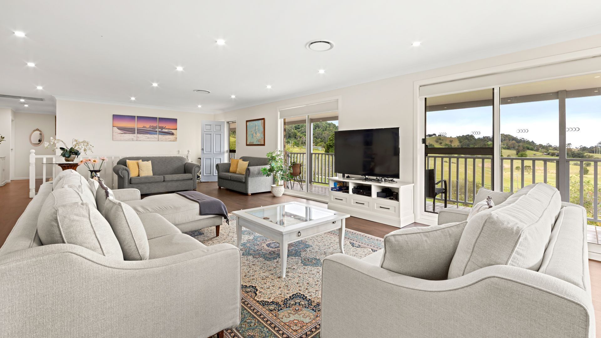 A spacious living room with a large TV, comfortable seating, and a balcony with a scenic view.