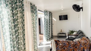 A modern living room with a sofa, a TV mounted on the wall, and a fan. - VILLA LAZUREA located in the heart of Terre-Sainte on the main avenue (Saint-Pierre)