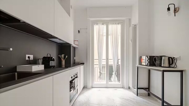 A modern kitchen with a dark countertop, white cabinets, and a built-in oven. There is a small table with a kettle and a toaster on it. - luxury suite Como (Como)