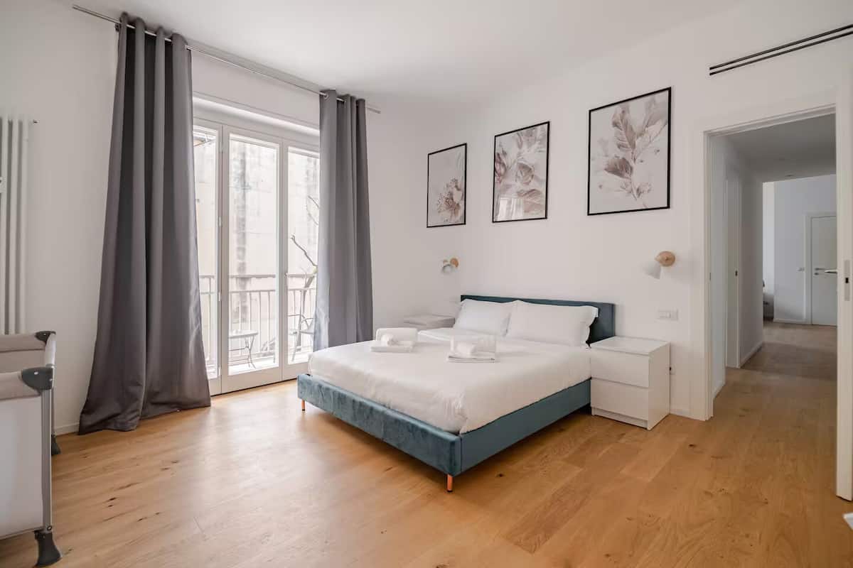 A modern bedroom with a large bed, bedside tables, and a balcony with curtains.