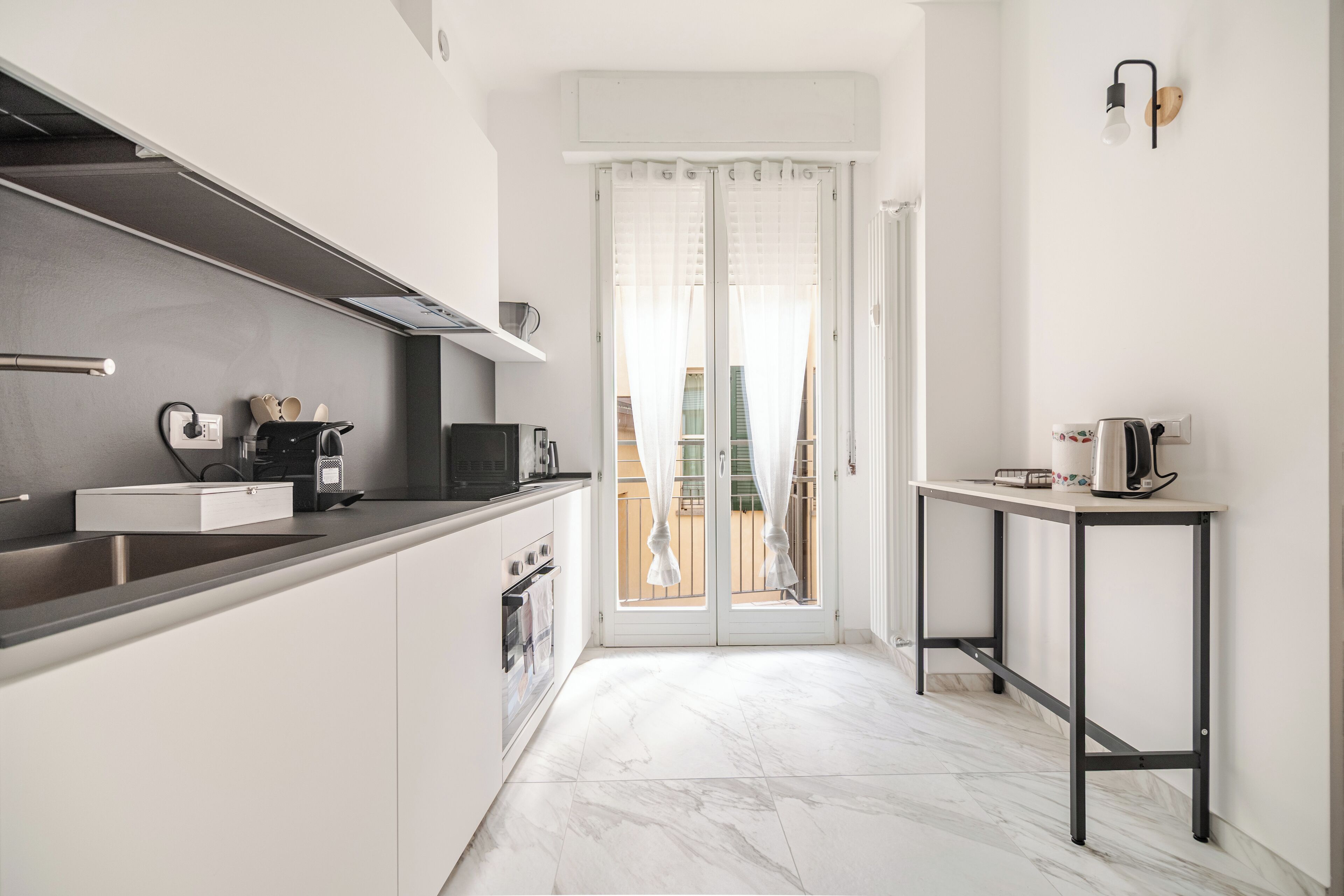 Una cocina moderna con armarios blancos, encimera negra y suelo de mármol.