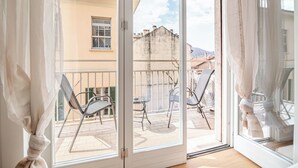 A balcony with two chairs and a table, a sliding glass door, and a view of buildings and a mountain in the background. - luxury suite Como (Como)