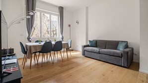 A modern living room with a grey sofa, a dining table with chairs, and a large window with curtains. - luxury suite Como (Como)