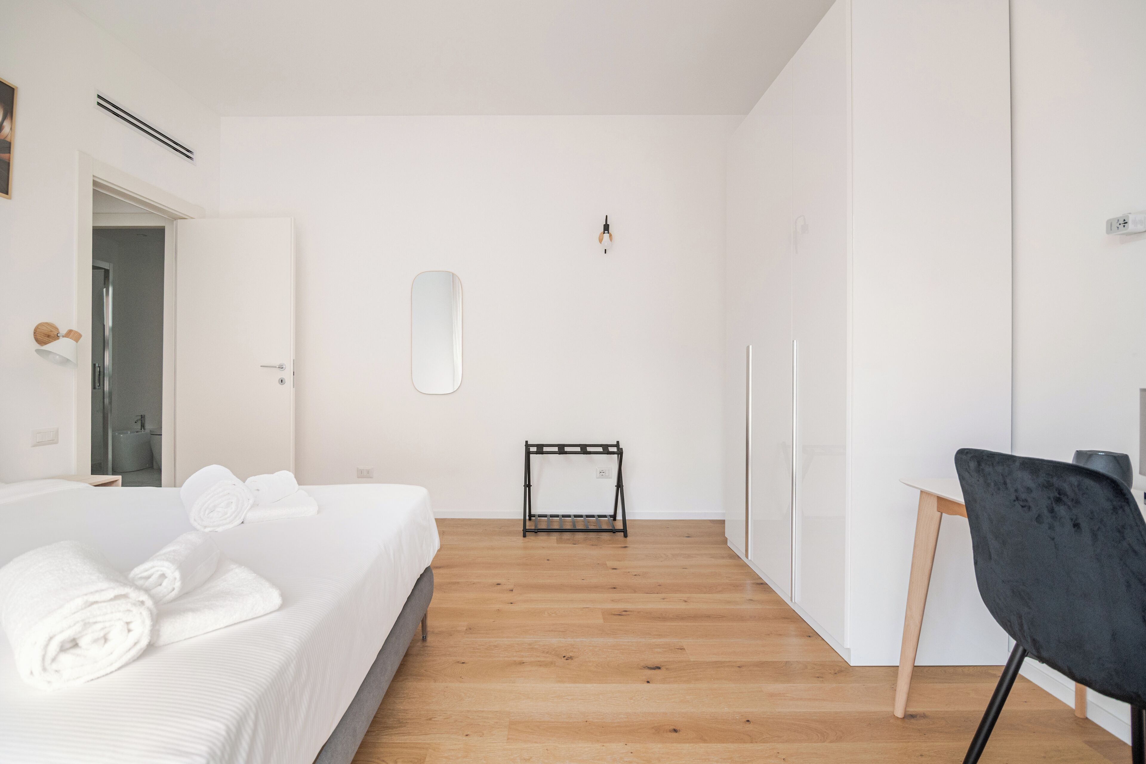 Ein modernes Hotelzimmer mit einem ordentlich bezogenen Bett, einem kleinen Schreibtisch und einem Stuhl.