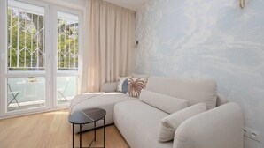 Un salon moderne avec un canapé d’angle, une petite table noire et un balcon doté de portes vitrées et de chaises.