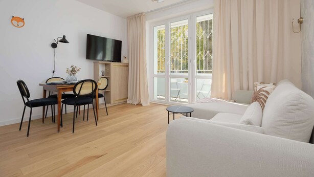 Un salon moderne comprenant un canapé, une table à manger, des chaises, un téléviseur et de grandes fenêtres avec des rideaux.